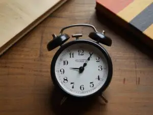 Relógio sobre uma mesa marrom com livros ao lado, representando disciplina, gestão do tempo e hábitos diários para alcançar o sucesso, mesmo sem motivação