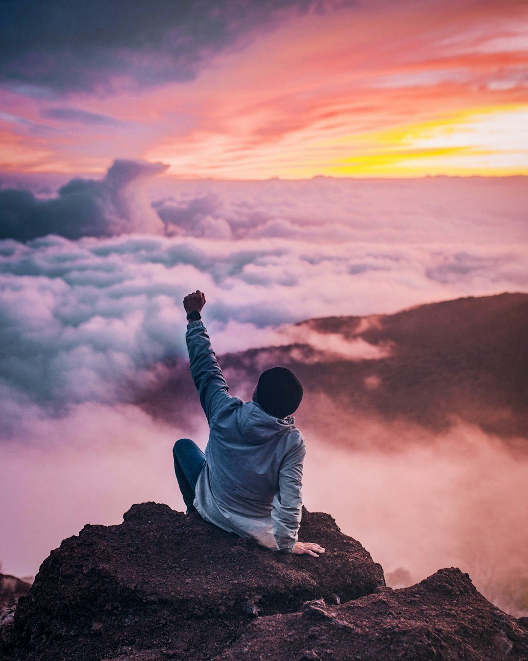 Pessoa contemplando o horizonte no topo de uma montanha ao nascer do sol simbolizando foco e vitória